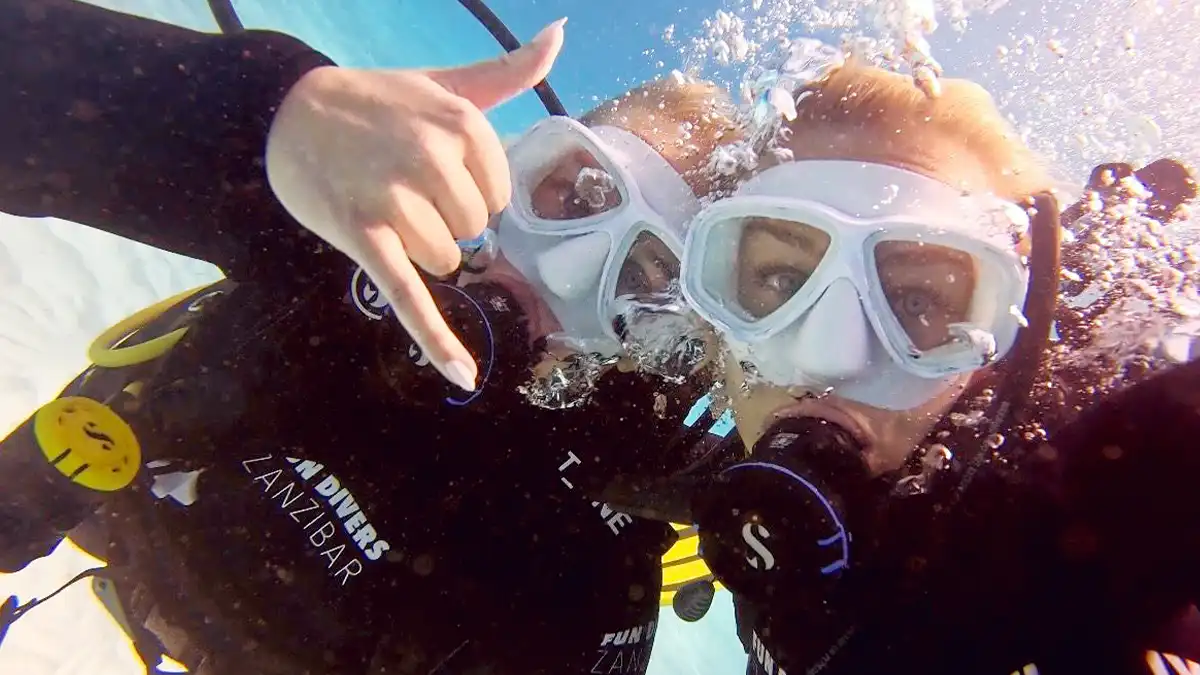Scuba divers giving a shaka sign underwater at Mnemba Island while diving Zanzibar
