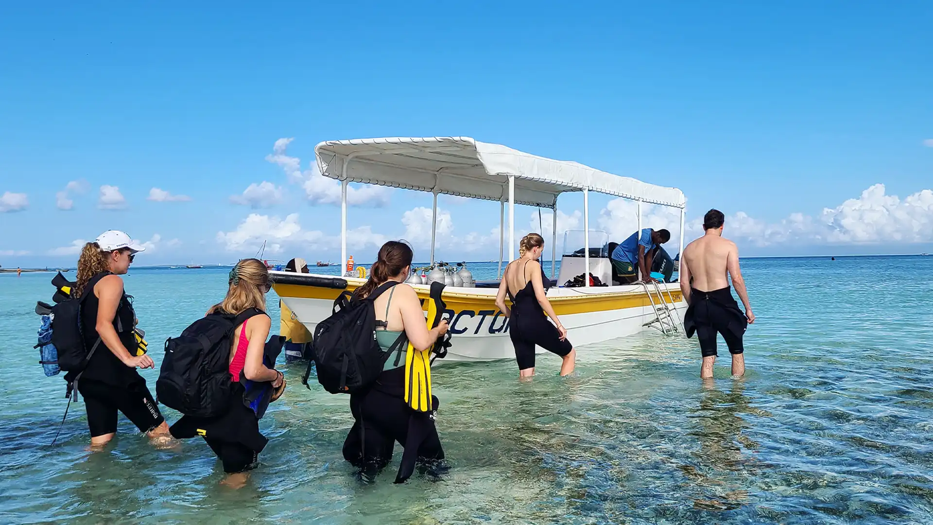Divers boarding a shaded dive boat at Nungwi Beach while diving Zanzibar