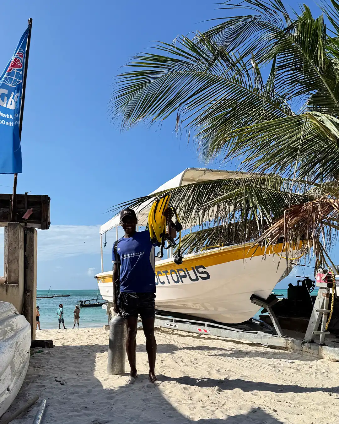 Nungwi Dive Center staff member with diving equipment on the beach in front of a dive boat in Zanzibar