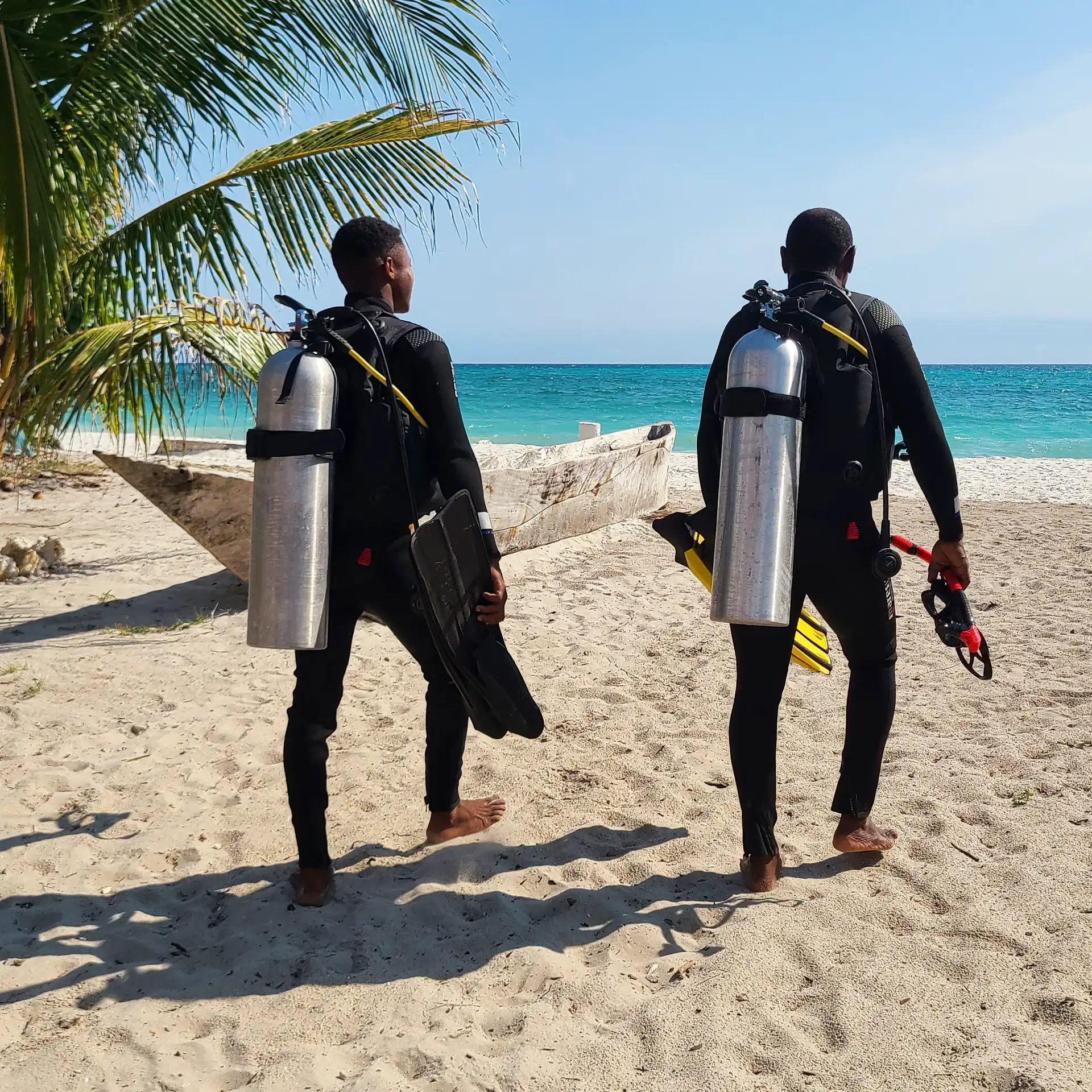 Scuba divers walking on the white sand beach toward the ocean in Makangale