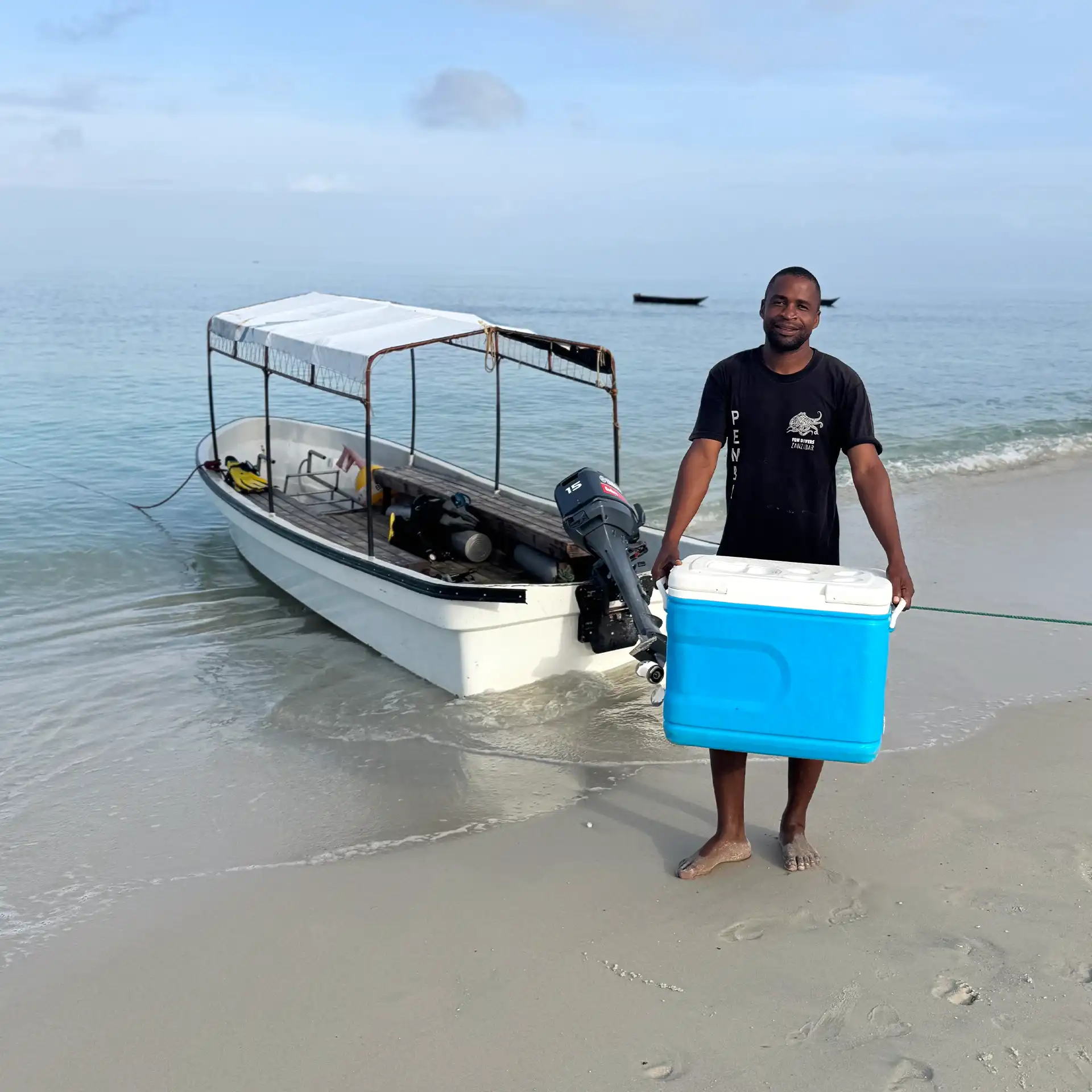 Dive crew member preparing a small shaded traditional dive boat on the beach in Pemba Island