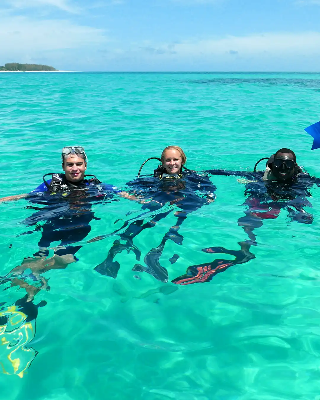 Scuba divers and PADI instructor surfacing in crystal clear waters at the Mnemba dive site in Zanzibar.