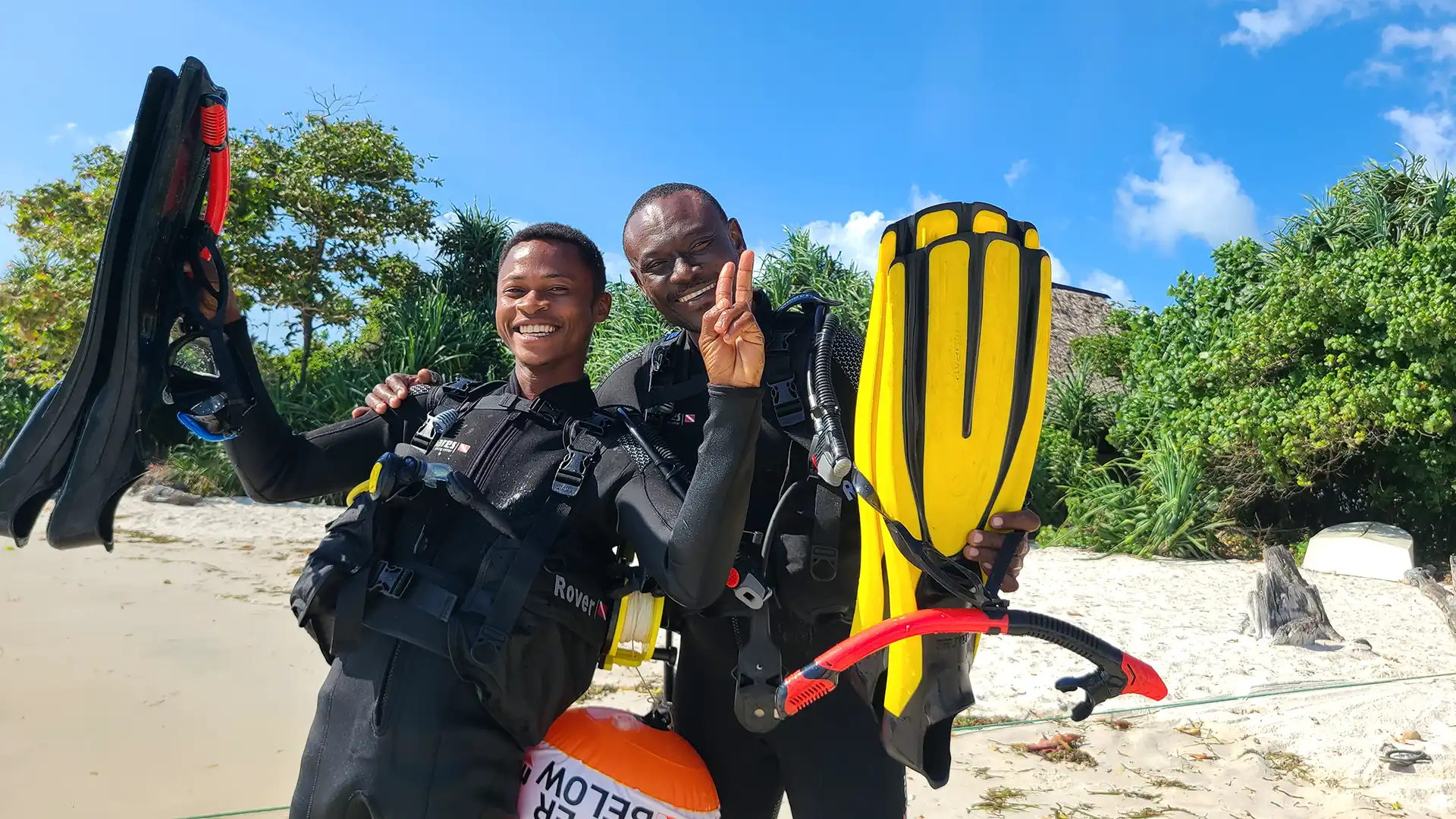 Smiling PADI dive instructor holding flippers and gear on the beach of Pemba Island
